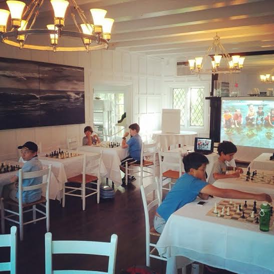 Students gathered around chess boards for a group lesson